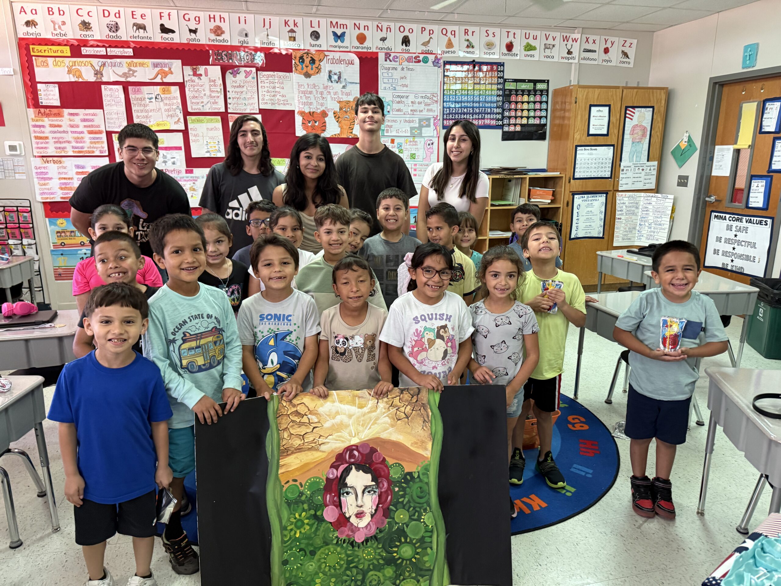 Elementary students and student volunteers posing together in a decorated classroom.