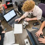 Students gather around a computer monitor in an engineering classroom