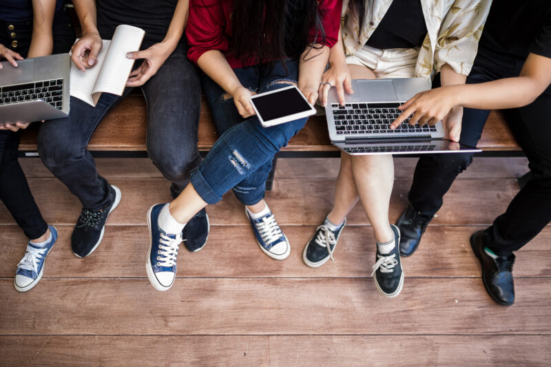 Students on a bench with laptops and digital devices